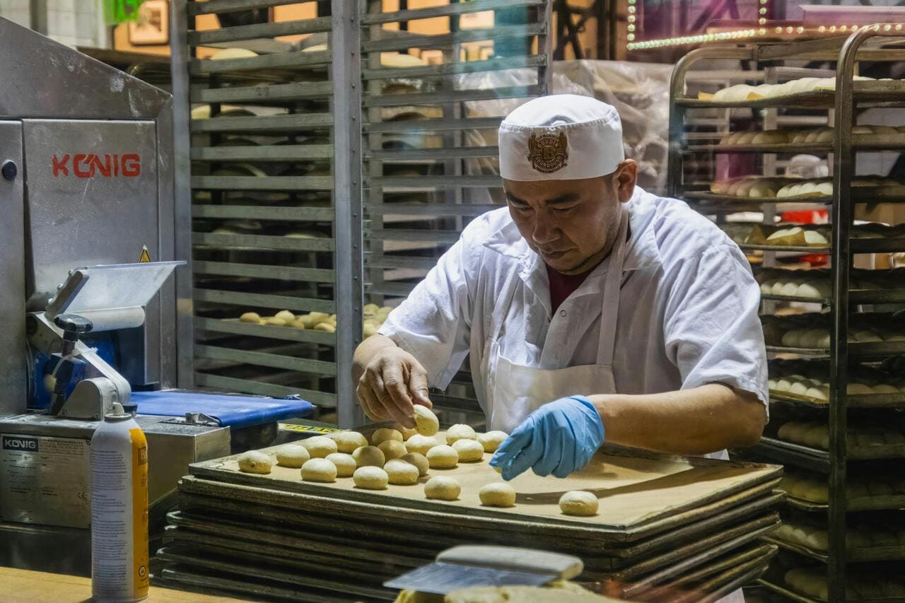 Pekar u beloj uniformi oblikuje loptice testa na plehu